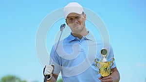 Handsome golfer posing with club and golden cup in hands, winner, triumph