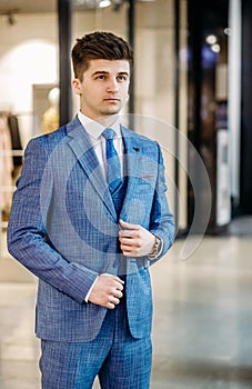 Handsome graceful man in stylish blue suit and tie and white shirt posing. Full length.