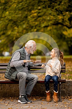 Grandfather playing red hands slapping game with his granddaughter in park on autumn day