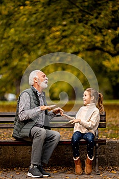 Grandfather playing red hands slapping game with his granddaughter in park on autumn day