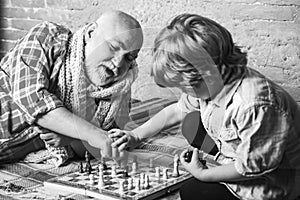 Handsome grandpa and grandson are playing chess while spending time together at home. Chess hobbies - granddad with