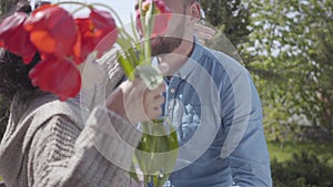 Handsome grandson visiting his grandmother, bringing her bouquet of tulips. The bearded man hugging his granny. People