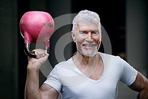 Handsome gray haired senior man with kettlebell weight in his hand. Sport and health care concept