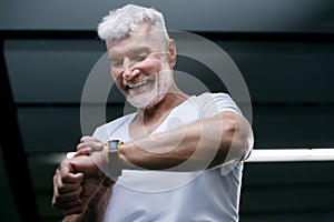 Handsome gray haired senior man looking at sport watch in his hand. Sport and health care concept