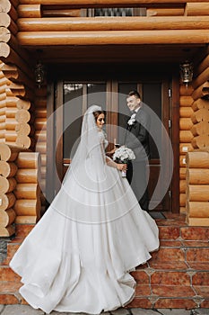 Handsome groom and charming bride stay together near modern wooden house