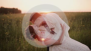 Handsome groom holds his beautiful bride in his arms, kissing her. Wedding at sunset in a beautiful place in nature