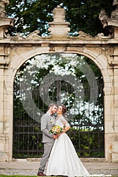 Handsome groom hugging beautiful bride with bouquet in romantic european park