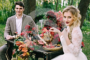 The handsome groom sit at the festive table on blurred bride background. Autumn wedding