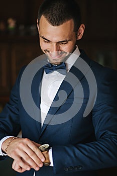 Handsome groom in stylish dark blue suit with bow tie