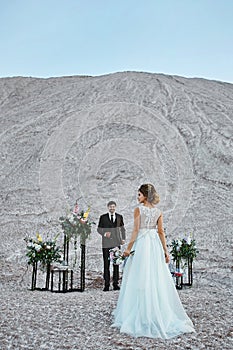 Handsome groom in stylish suit waiting for the bride in a luxurious dress at the place of outdoors wedding ceremony