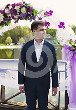 Handsome groom waiting for bride under floral arch at ceremony