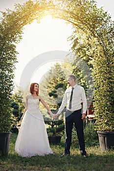 Handsome groom holds the bride`s hand near green flower archway