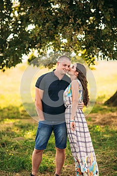 Handsome guy and an attractive girl hug each other near a large green tree. Love story