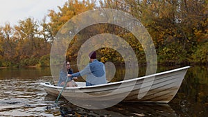 A handsome guy and a beautiful girl swim in a boat on a lake in a fairy autumn forest