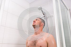 Handsome guy with closed eyes standing under flowing water in sh