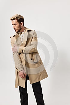 handsome guy in a coat parodies on a light background and looks to the side