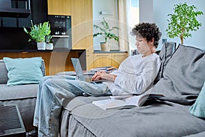 Handsome guy college student studying at home typing on laptop, sitting on sofa