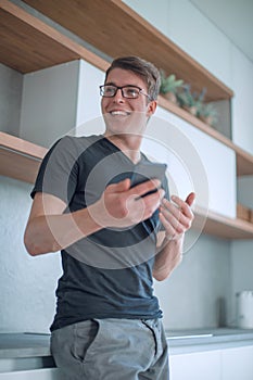 Handsome guy with a Cup of coffee and a smartphone standing in the kitchen