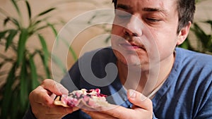 A handsome guy with great pleasure eats a delicious sweet pizza with apple pieces, berries, almond slices and condensed milk.