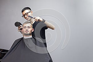 Handsome guy has a haircut in a barbershop, a Kazakh barber dries a client`s hair dryer against a gray wall, a hairdresser makes