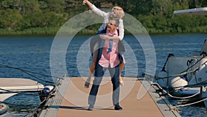 Handsome guy holds girl on his back and makes selfie at the pier