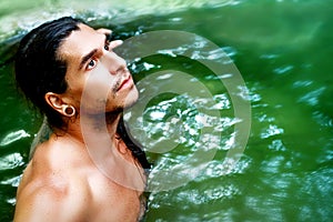 A handsome guy with long hair and piercings on waterfalls in a rain forest against a background of green water photo