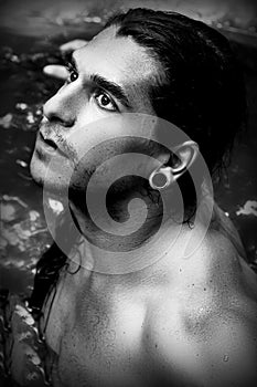 A handsome guy with long hair and piercings on waterfalls in a rain forest. Black and white photo