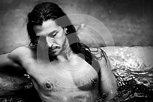 A handsome guy with long hair and piercings on waterfalls in a rain forest. Tarzan concept. Black and white photo.