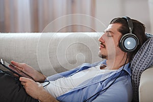 Handsome guy lying on sofa with tablet and headphones