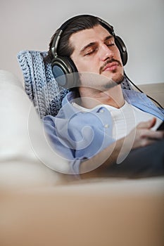 Handsome guy lying on sofa with tablet and headphones
