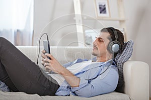 Handsome guy lying on sofa with tablet and headphones