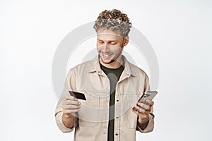 Handsome guy pays with credit card, placing an order in application on mobile phone, making purchase in online store