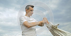 Handsome guy puts on a shirt against the background of the sky. Men`s fashion, unity with nature