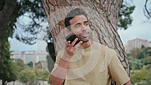 Handsome guy recording audio message on smartphone at green park close up.