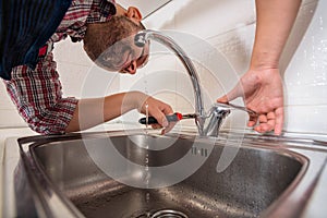 Handsome guy repair pipes on sink in the kitchen