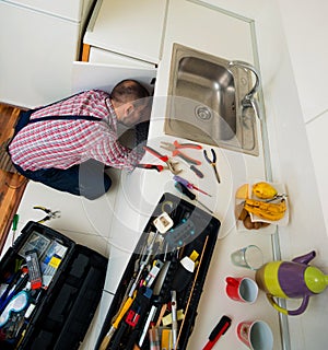 Handsome guy repair pipes on sink in the kitchen