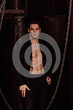A handsome guy with an shirt stands in a dark room near chains and pipes