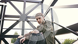 Handsome guy sitting on iron stairs look straight to camera. Outdoor lifestyle portrait of a handsome young caucasian