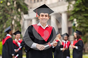 Handsome guy student in graduation costume showing diploma