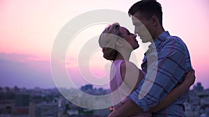 Handsome guy tenderly embracing his beautiful lady on open terrace, cityscape