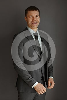 A handsome guy in a trendy grey suit, checkered shirt, and tie posing over grey background. Young handsome businessman