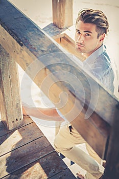 Handsome guy with trendy hairstyle going down wooden stairs while looking.