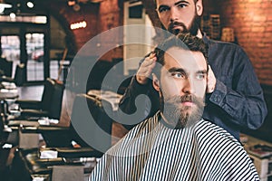 Handsome guy is turned his head to the right by hairstylist. Hairdreser is trying to get a good hairstyle for his