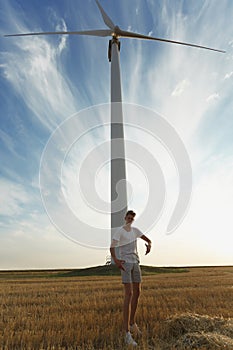 Handsome guy on a windmill background. Male teenager supporting alternative energy sources. Progressive youth concept.