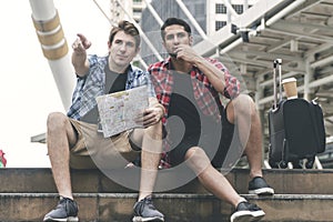 Handsome guys searching for direction using map paper while sitting on stairs in city. Tourist young man using map
