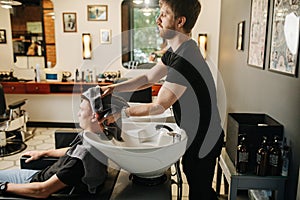 Handsome hairdresser drying client`s hair with a towel in a barber shop