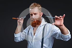 Handsome hairstylist or hairdresser bearded man barber cut beard hair with retro blade razor and scissors to do haircut