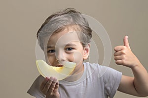 handsome, happy boy holding ripe, sweet, juicy, fresh slice of melon and shows thumbs up. smiling child doing OK sign