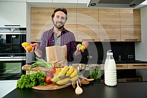 Handsome happy Caucasian man in casual wear holding raw fresh fruits in hands and smiling looking at camera while standing at