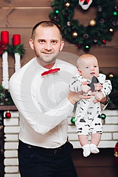 Handsome happy father in white shirt and tie holding little son by hands.